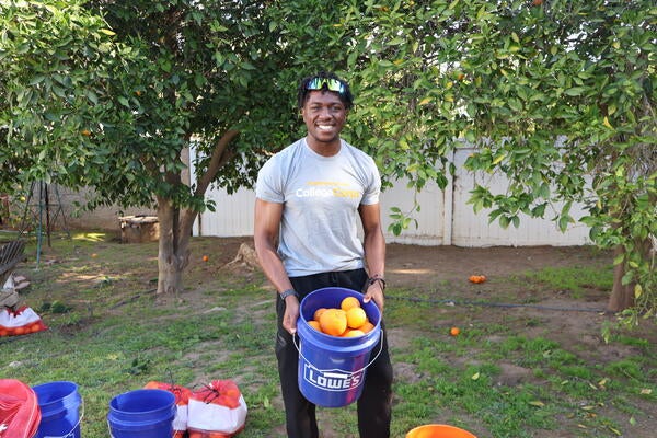 Student standing holding oranges in a bucket 